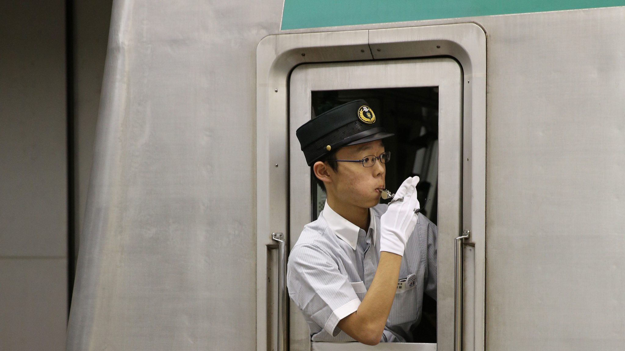 Tokio. De treinbegeleider seint: klaar voor vertrek. Witte handschoenen zijn standaard onderdeel van het uniform. 