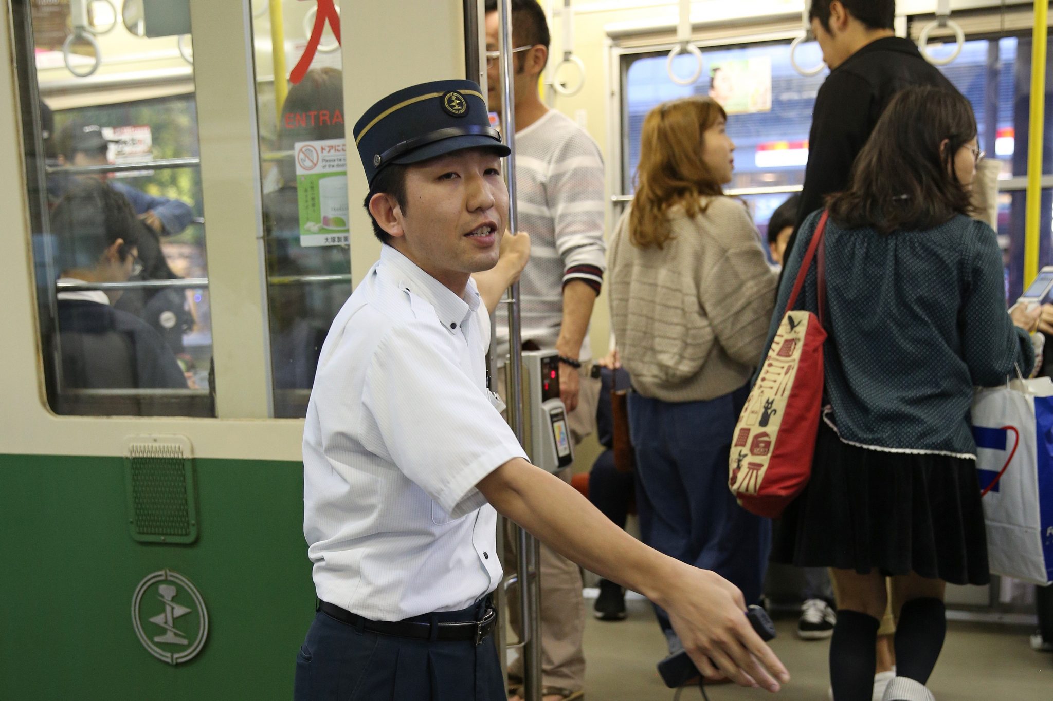 Hiroshima. Bij een drukke tramhalte maant een ‘opzwaaier’ reizigers snel in te stappen. 