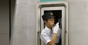 Tokio. De treinbegeleider seint: klaar voor vertrek. Witte handschoenen zijn standaard onderdeel van het uniform. 